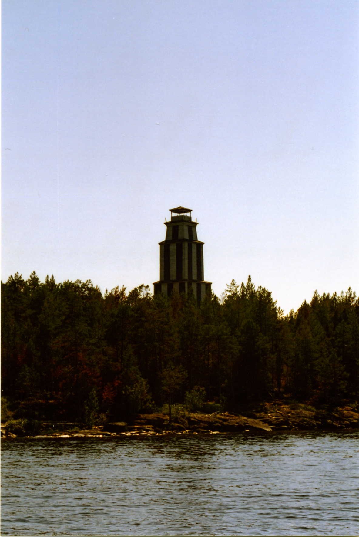 The Vasilisin lighthouse tower seen from the water across a tree-lined shore on Lake Onega.